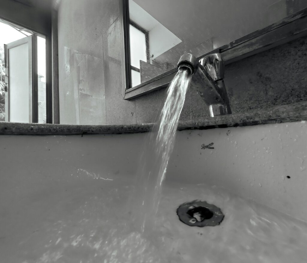 Monochrome close-up of water flowing from a faucet into a sink with selective focus.